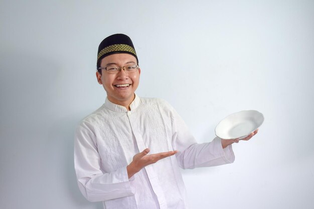 Uomo musulmano asiatico che indossa occhiali e un panno bianco che indica un piatto vuoto per il digiuno di Ramadan