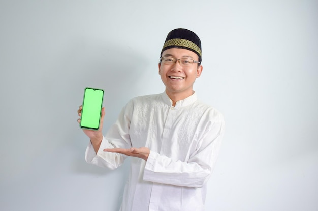 Uomo musulmano asiatico con gli occhiali e un panno bianco che punta al telefono posa per il Ramadan e l'Eid al-Fitr