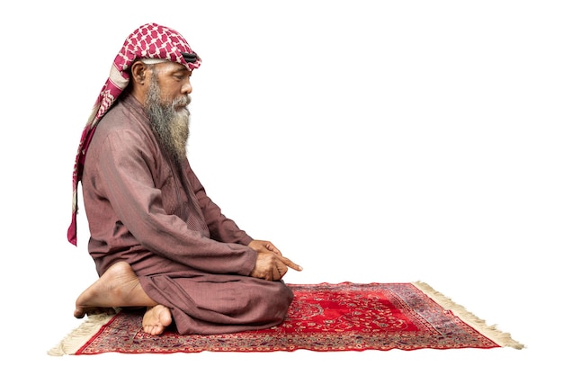 Uomo musulmano con barba che indossa keffiyeh con agal in posizione di preghiera salat sul tappeto di preghiera