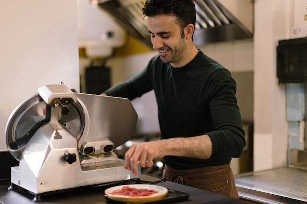 Uomo nella cucina del ristorante che prepara le fette di carpaccio usando l'affettatrice