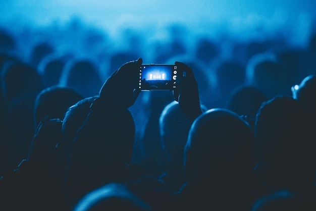 Uomo nella folla che fotografa il palco illuminato attraverso lo smartphone al teatro