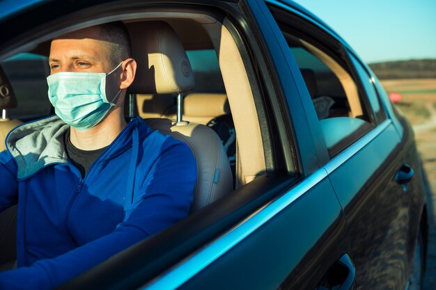 Uomo nella mascherina medica che conduce un'automobile