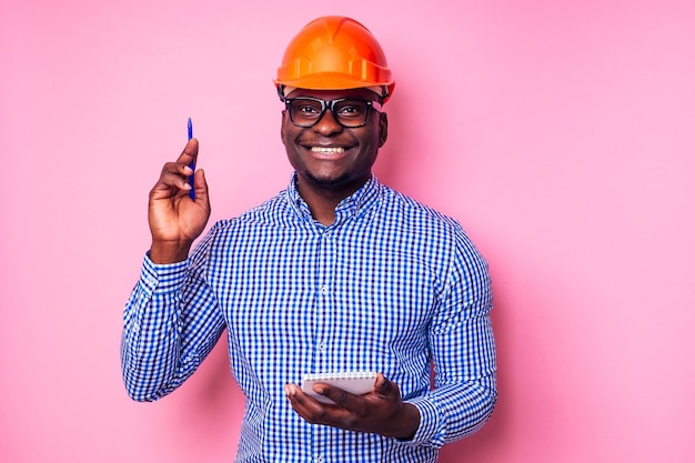 Uomo nero afroamericano che annota le idee in un taccuino dipinge il muro in colore rosa. Casa felice del costruttore africano, architetto designer uomo d'affari indossa un casco casco. Capo giovane studente.