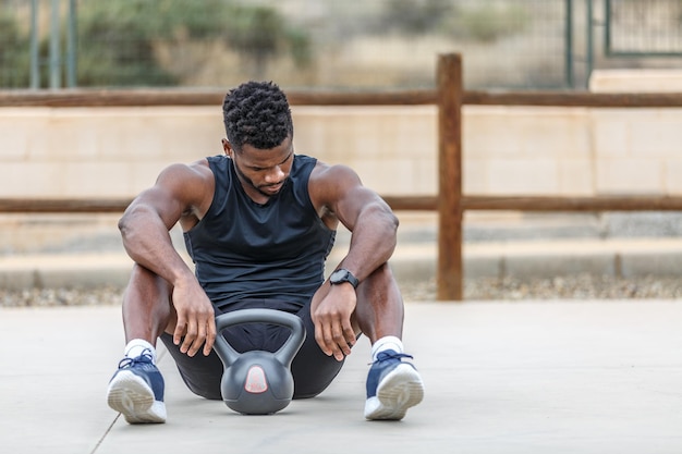 Uomo nero atletico che si riposa sul campo sportivo con la kettlebell