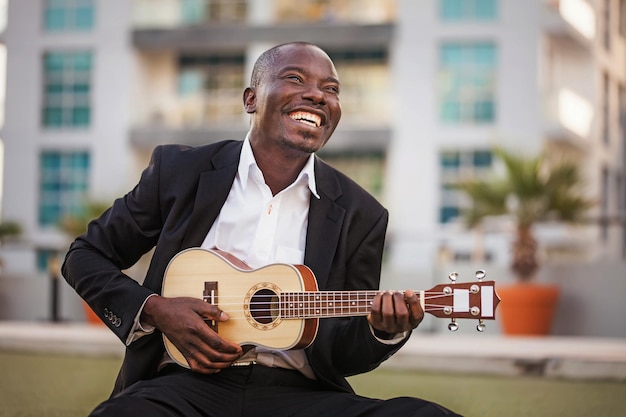 Uomo nero sorridente che indossa abiti formali che suonano l'ukulele