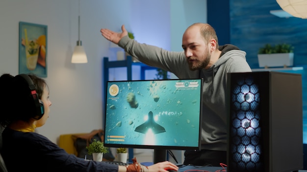 Uomo nervoso che urla alla donna mentre sta giocando a un videogioco sparatutto spaziale su un potente computer RGB e a una competizione online in streaming. Pro cyber con auricolare che si esibisce durante il torneo virtuale