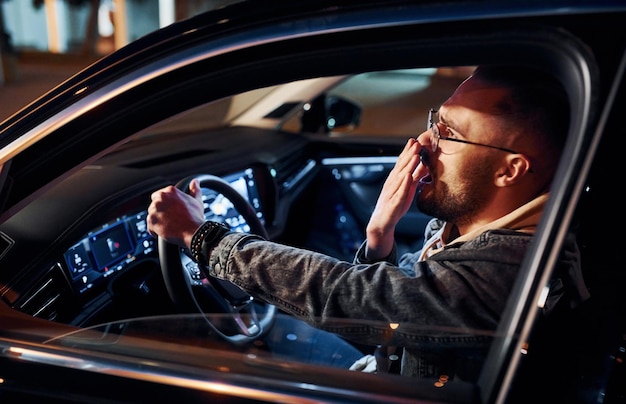 Uomo non rasato bello stanco in abiti alla moda che guida la sua automobile