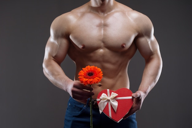 Uomo nudo atletico che tiene in mano una gerbera rossa e una confezione regalo. Concetto di San Valentino