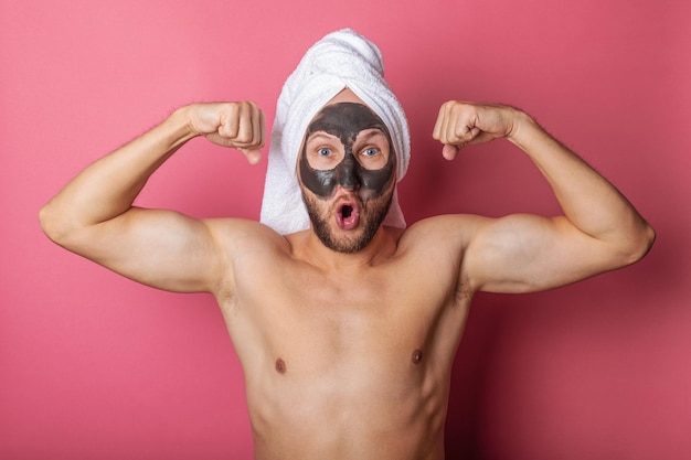Uomo nudo sorpreso con una maschera cosmetica sul viso che mostra i muscoli su uno sfondo rosa
