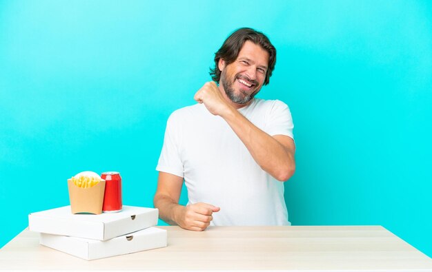 Uomo olandese anziano che mangia fast food seduto in un tavolo per celebrare una vittoria