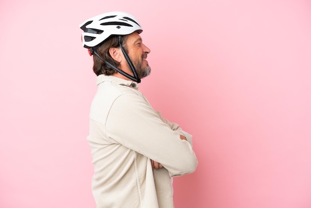 Uomo olandese anziano con casco da bici isolato su sfondo rosa in posizione laterale
