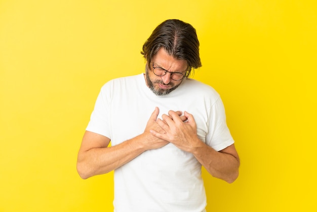 Uomo olandese anziano isolato su sfondo giallo che ha un dolore al cuore