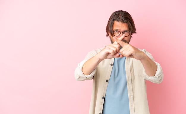 Uomo olandese anziano isolato su sfondo rosa che fa un gesto di arresto con la mano per fermare un atto