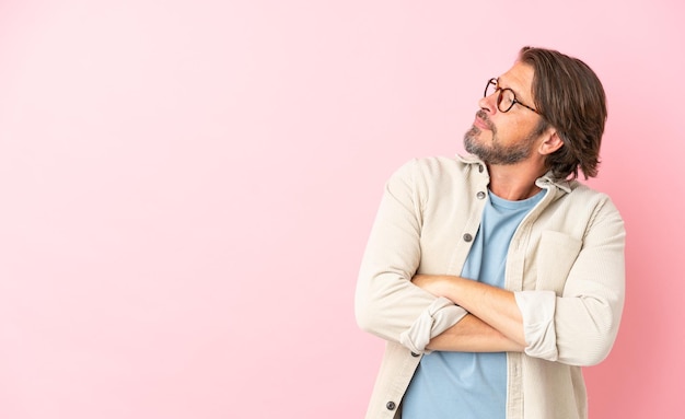 Uomo olandese anziano isolato su sfondo rosa tenendo le braccia incrociate