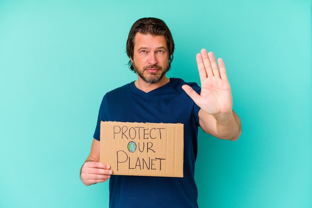 Uomo olandese di mezza età che tiene un cartello di protezione del nostro pianeta isolato sulla parete blu in piedi con la mano tesa che mostra il segnale di stop, impedendoti.