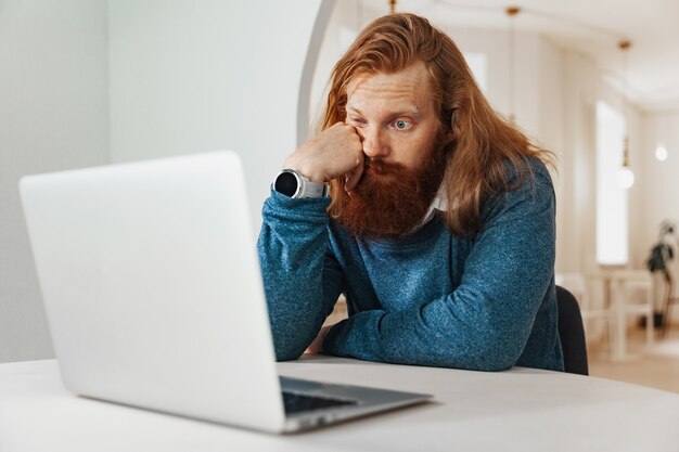 Uomo pensieroso e stanco che lavora al computer portatile in caffè