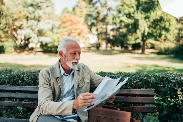 Uomo pensionato leggendo giornali nel parco.