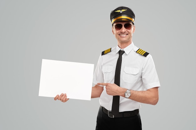 Uomo pilota felice che mostra carta bianca in bianco