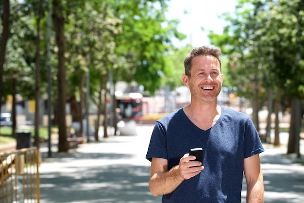 Uomo più anziano che sta fuori con il cellulare che sorride sul marciapiede