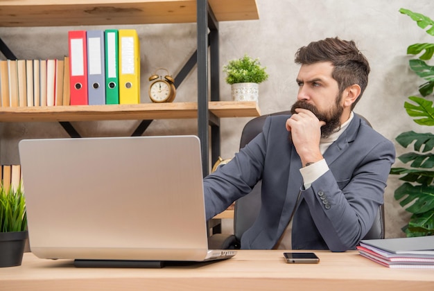 Uomo premuroso che utilizza il computer portatile che lavora al decisore della scrivania dell'ufficio