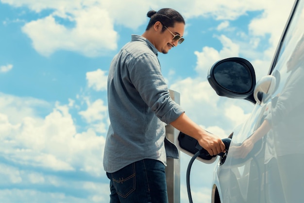 Uomo progressista con auto EV collegata con sfondo cloudscape punto di ricarica