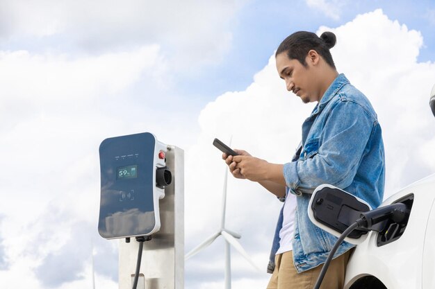 Uomo progressista con la sua auto EV e turbina eolica come concetto di energia rinnovabile