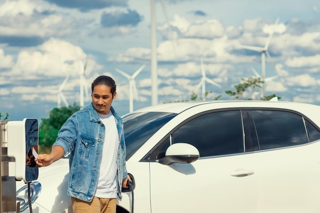 Uomo progressista con la sua auto EV e turbina eolica come concetto di energia rinnovabile