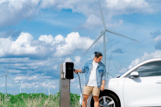 Uomo progressista con la sua auto EV e turbina eolica come concetto di energia rinnovabile