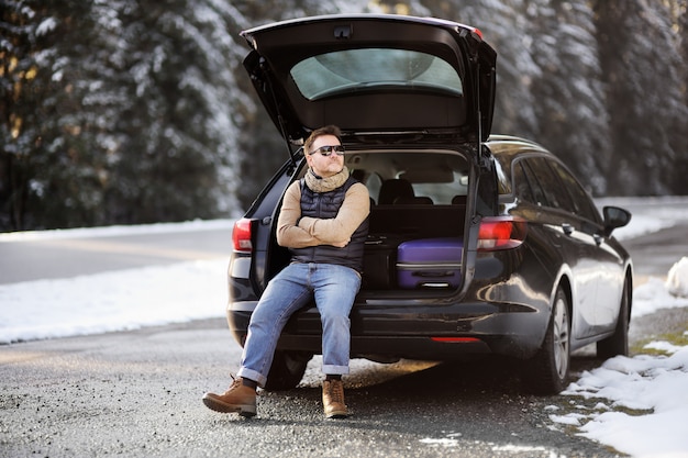 Uomo pronto ad andare in vacanza e rilassarsi nel bagagliaio aperto di una macchina prima di un viaggio