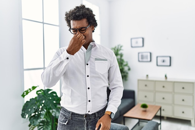 Uomo psicologo africano presso l'ufficio di consultazione che sente l'odore di qualcosa di puzzolente e disgustoso odore intollerabile che trattiene il respiro con le dita sul naso cattivo odore