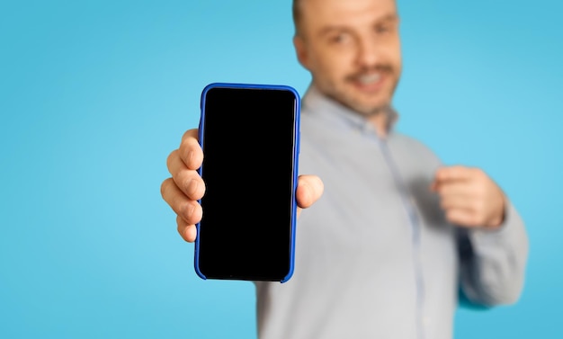 Uomo pubblicità offerta mobile che mostra lo schermo dello smartphone su sfondo blu