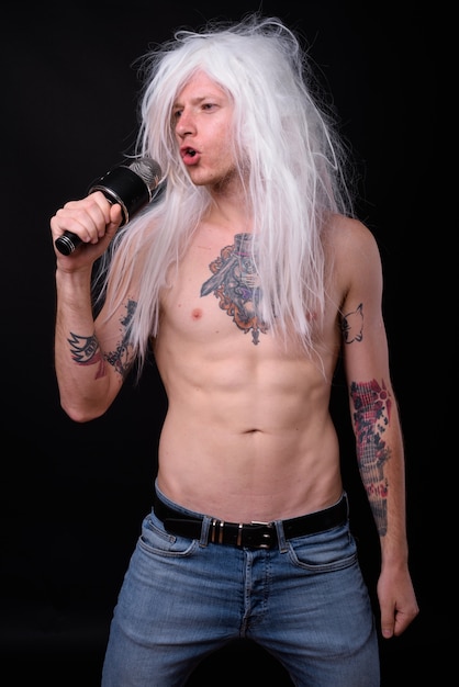 uomo ribelle come punk rocker che indossa parrucca a torso nudo contro il nero