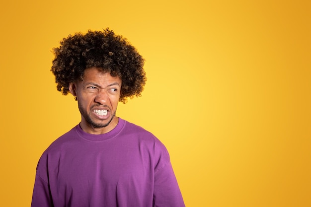 Uomo riccio afroamericano adulto triste arrabbiato in maglietta viola che esamina spazio vuoto
