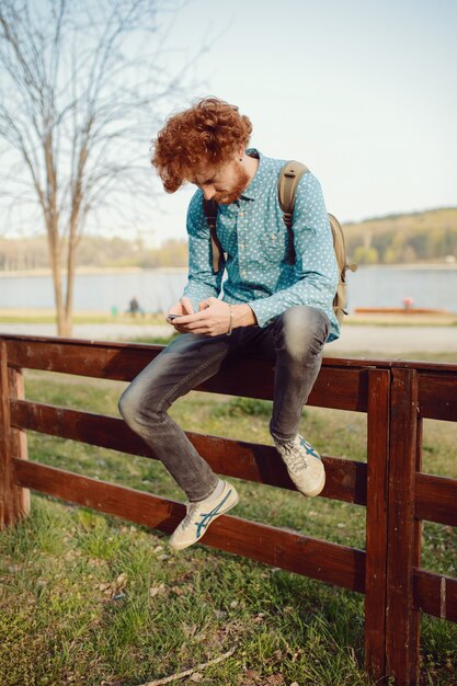 Uomo riccio dello zenzero che per mezzo dello smartphone su bello paesaggio