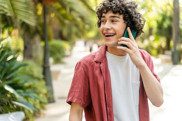 Uomo riccio sereno che parla al cellulare mentre cammina con un sorriso felice in città