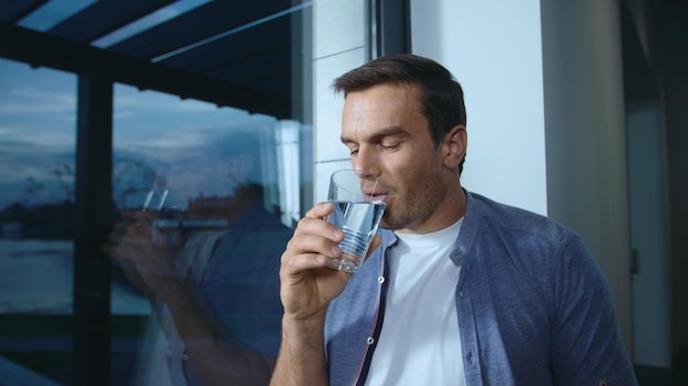 Uomo rilassato che beve acqua vicino alla finestra Persona di sesso maschile assetata che beve acqua