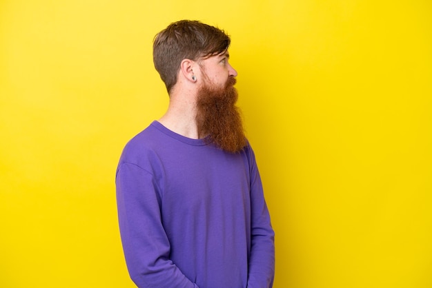 Uomo rosso con barba isolato su sfondo giallo che guarda di lato