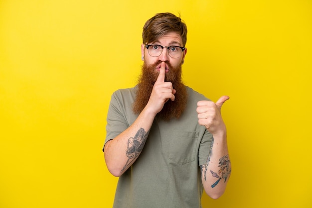 Uomo rosso con barba isolato su sfondo giallo che punta di lato e fa gesto di silenzio