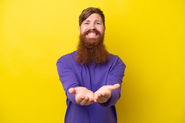 Uomo rosso con barba isolato su sfondo giallo che tiene copyspace immaginario sul palmo per inserire un annuncio