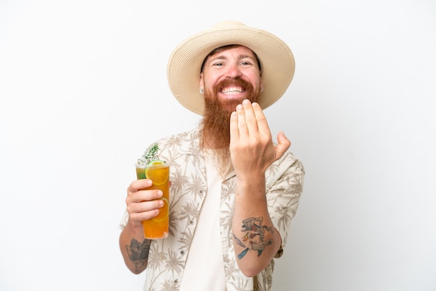 Uomo rosso con barba lunga che beve un cocktail su una spiaggia isolata su sfondo bianco che invita a venire con la mano Felice che tu sia venuto