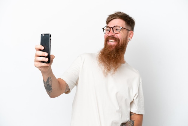 Uomo rosso con barba lunga isolato su sfondo bianco facendo un selfie