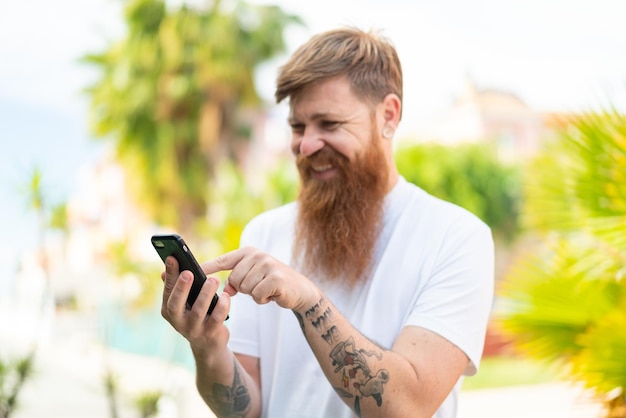 Uomo rosso con la barba che invia un messaggio o un'e-mail con il cellulare