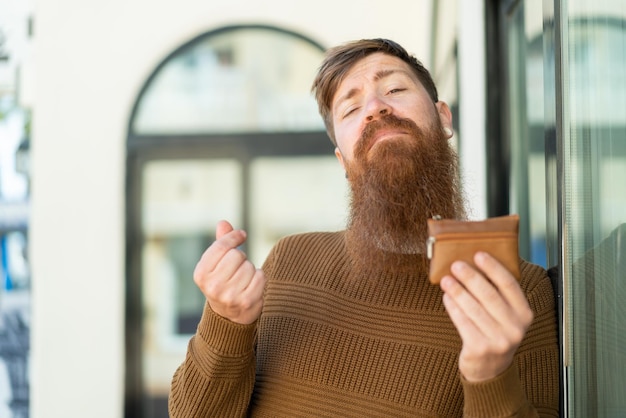 Uomo rosso con la barba che tiene il portafoglio con gesto di denaro