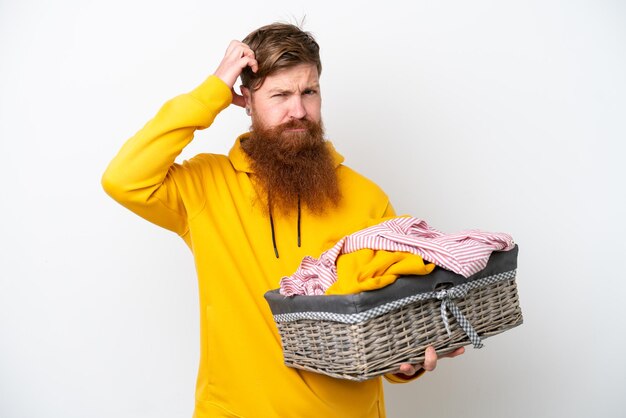 Uomo rosso con la barba che tiene un cesto di vestiti isolato su sfondo bianco con dubbi