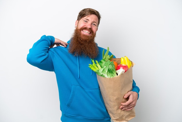 Uomo rosso con la barba che tiene una borsa della spesa isolata su sfondo bianco ridendo