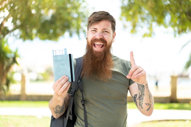 Uomo rosso con la barba in possesso di un passaporto all'aperto che indica una grande idea