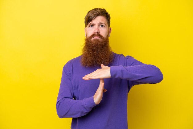 Uomo rosso con la barba isolato su sfondo giallo che fa un gesto di timeout