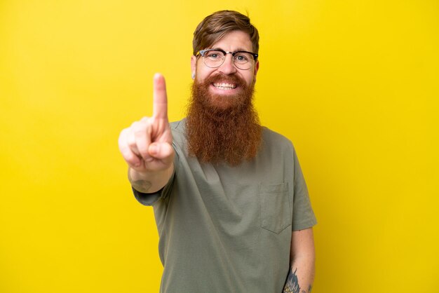 Uomo rosso con la barba isolato su sfondo giallo che mostra e alza un dito