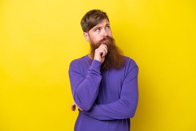 Uomo rosso con la barba isolato su sfondo giallo pensando a un'idea mentre guarda in alto