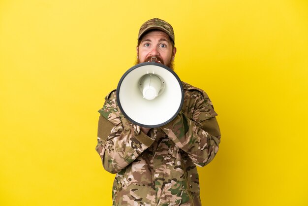 Uomo rosso militare sopra isolato su sfondo giallo che grida attraverso un megafono